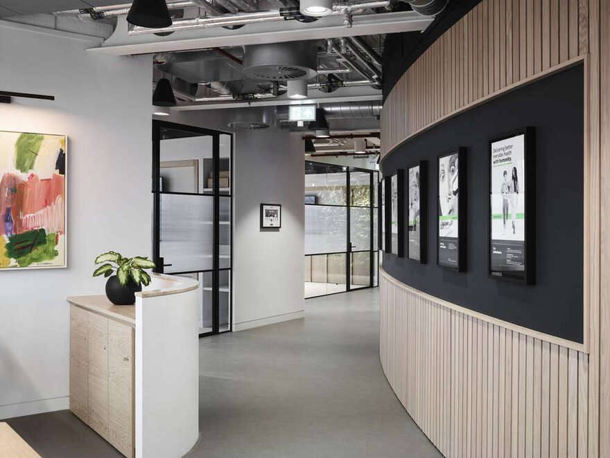 Curved oak-slatted wall with framed Haleon brand prints